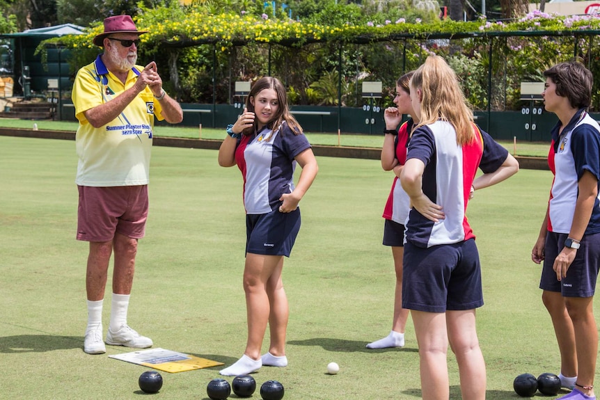 Students playing lawn bowls with senior coach.