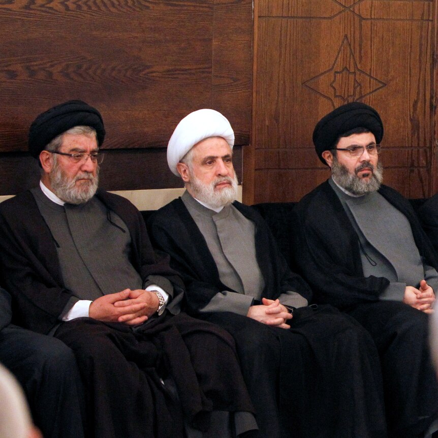 A row of three Hezbollah officials sitting down. They are wearing turbans.