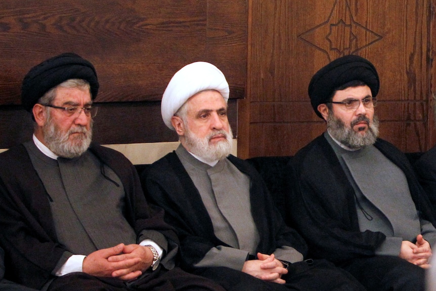 A row of three Hezbollah officials sitting down. They are wearing turbans.