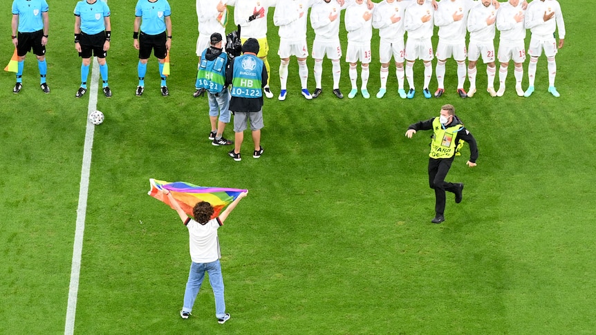 A person holding a rainbow flag faces the players during the playing of the Hungarian national anthem at Euro 2020.