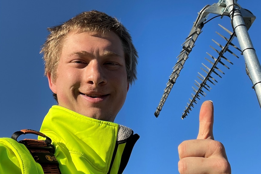 A selfie of a guy on a roof, next to an antenna.