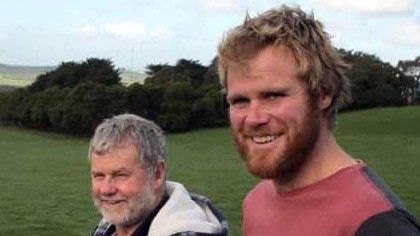 Two men smile as they stand in a green paddock.