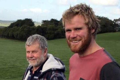 Two men smile as they stand in a green paddock.