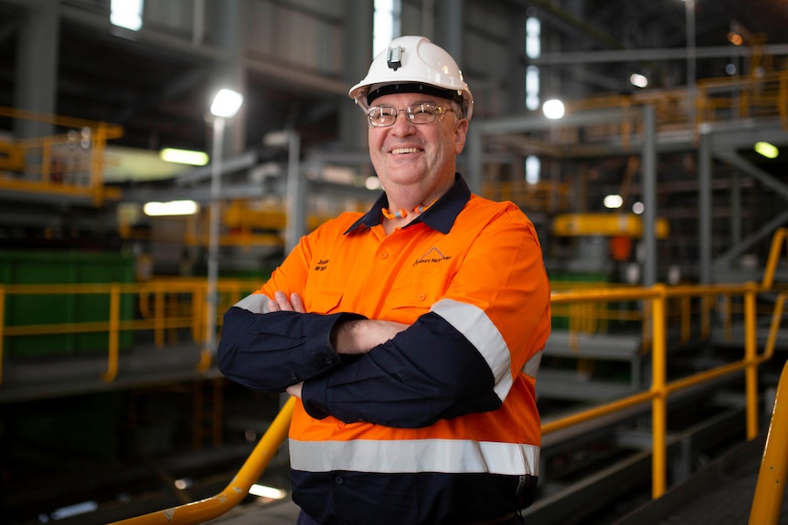 A man in a hard hat and a high-vis vest stands in front of machinery