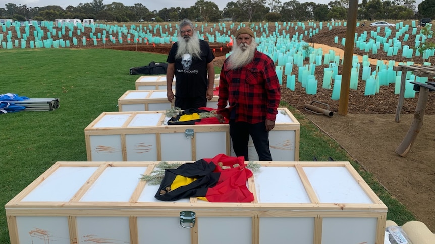Two men standing outside near four white coffin-sized boxes.