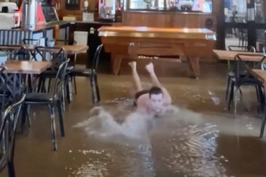 A man swimming in a flood-hit dining room.