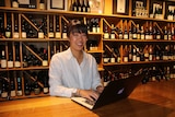 Bianca Welsh sits at a computer in front of a wine bar.