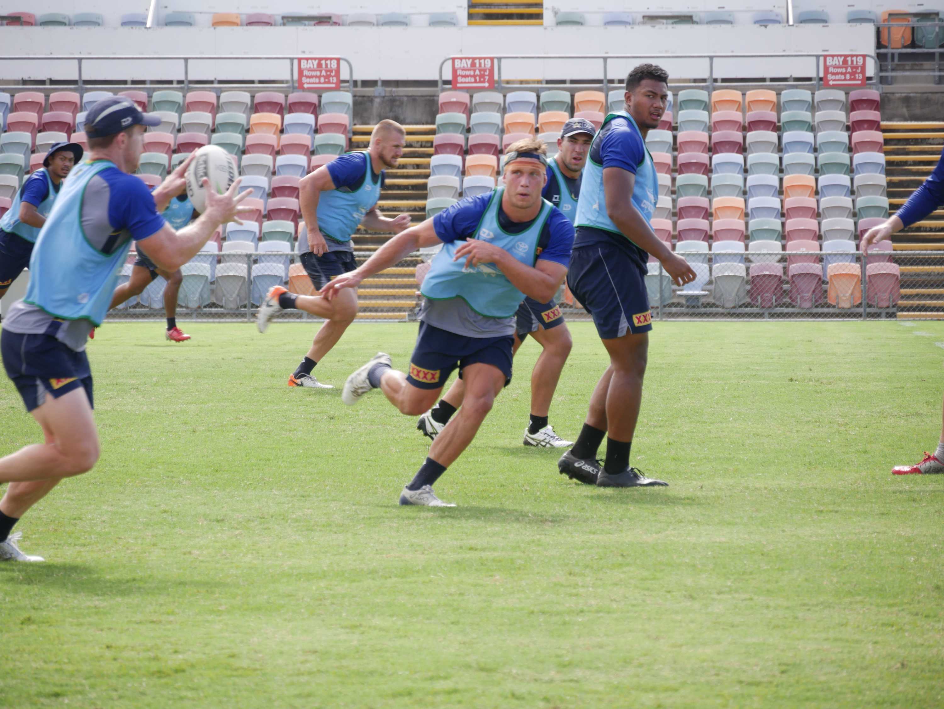 Young man wearing grey and blue shirt with blue bib passing a white football to another footballer in the same attire
