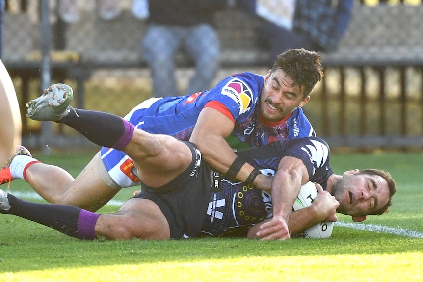 A Melbourne Storm NRL player is tackled by a Newcastle Knights opponent while holding the ball.