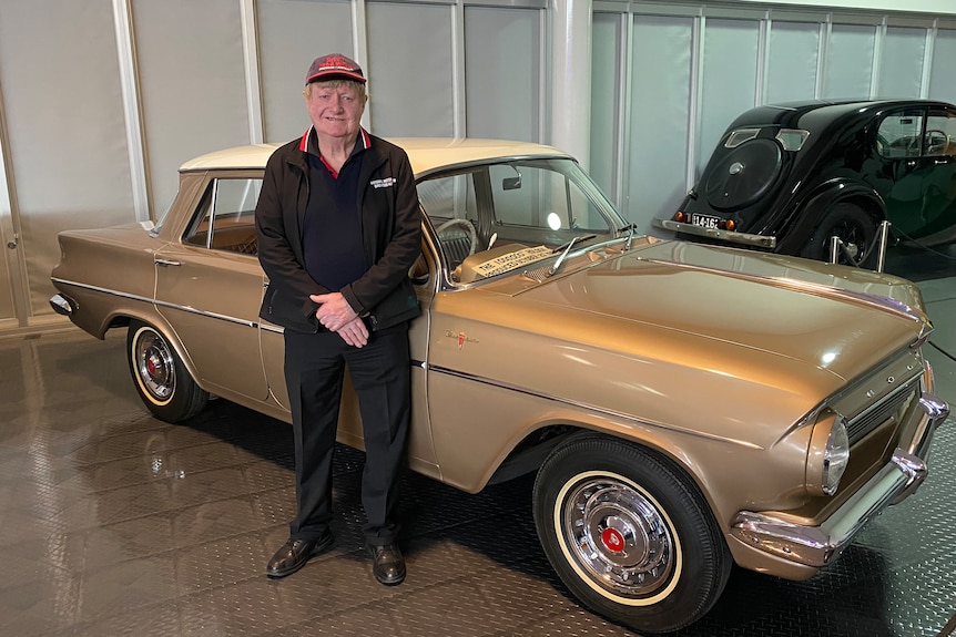 A man stands in front of a historic car