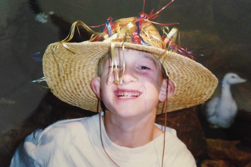 A smiling child in a hat with a goose in the background