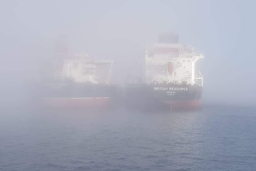 The sterns of two big ships covered in fog