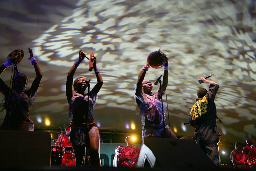 Three dancers on a stage with a singer 