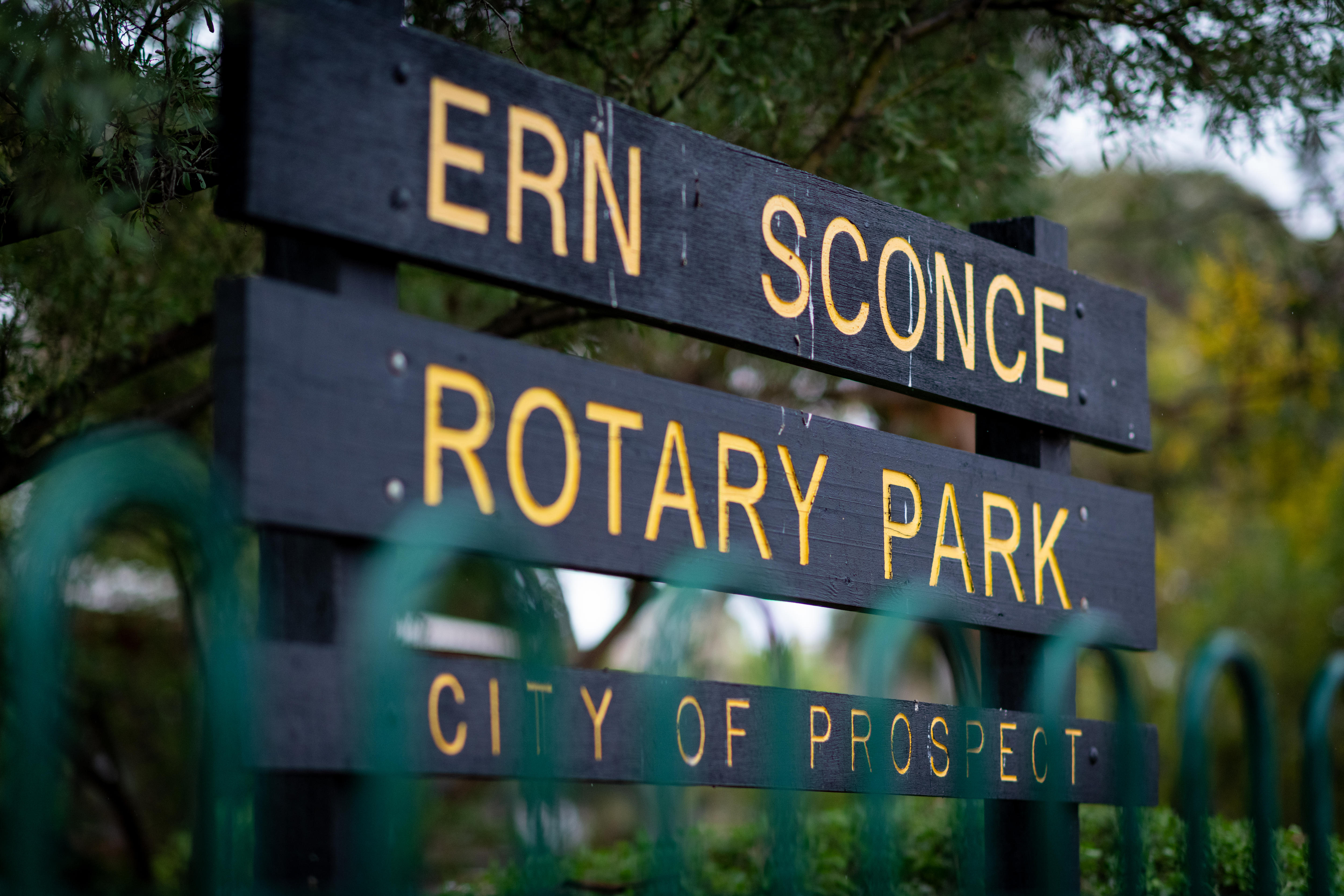 A sign reading Ern Sconce Rotary Park in front of trees and behind a green fence