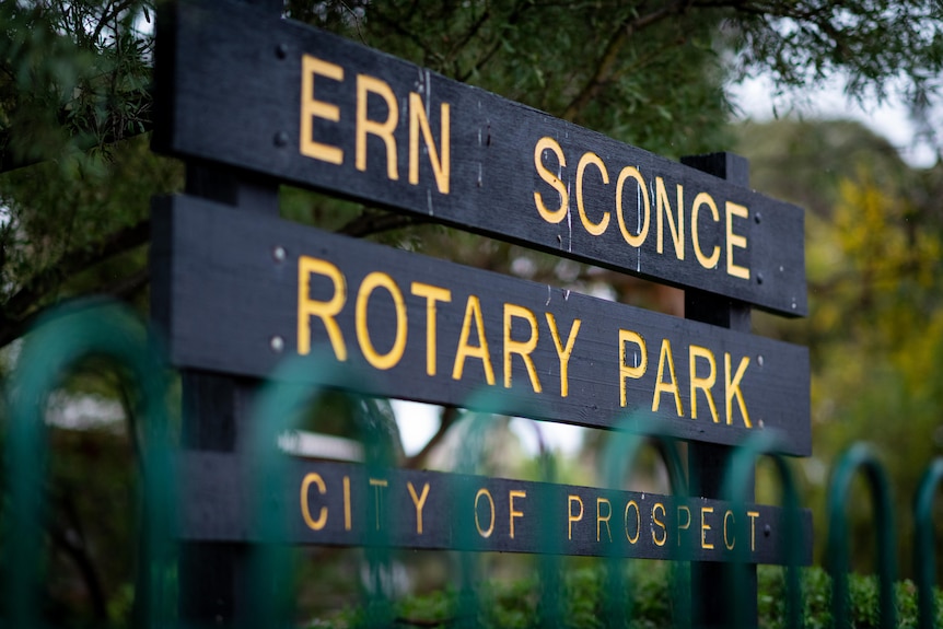 Табела с надпис Ern Sconce Rotary Park пред дървета и зад зелена ограда