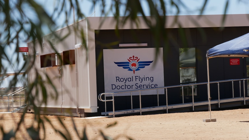 A modern building with a large sign reading 'Royal Flying Doctor Service' is framed by eucalyptus leaves. 