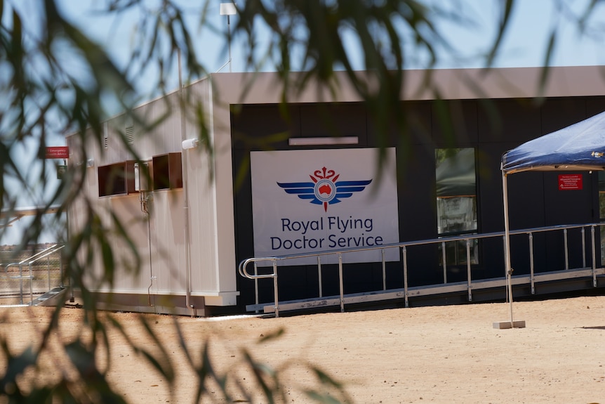 A modern building with a large sign reading 'Royal Flying Doctor Service' is framed by eucalyptus leaves. 