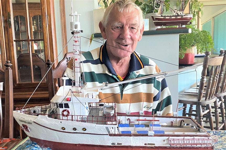 Man behind wooden model of white fishing boat