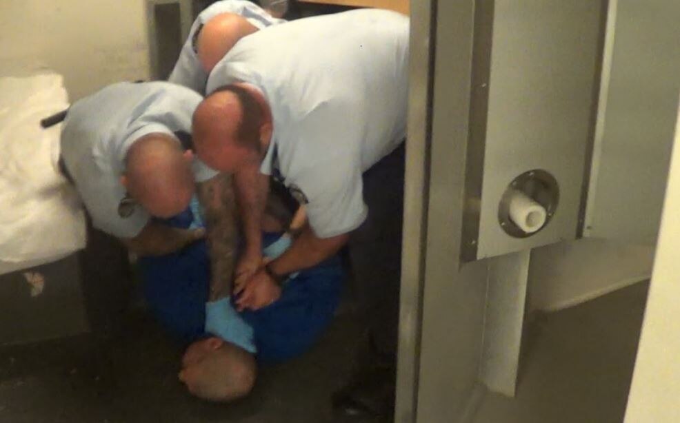 A man being held down by three prison guards.