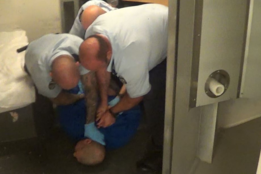 A man being held down by three prison guards.