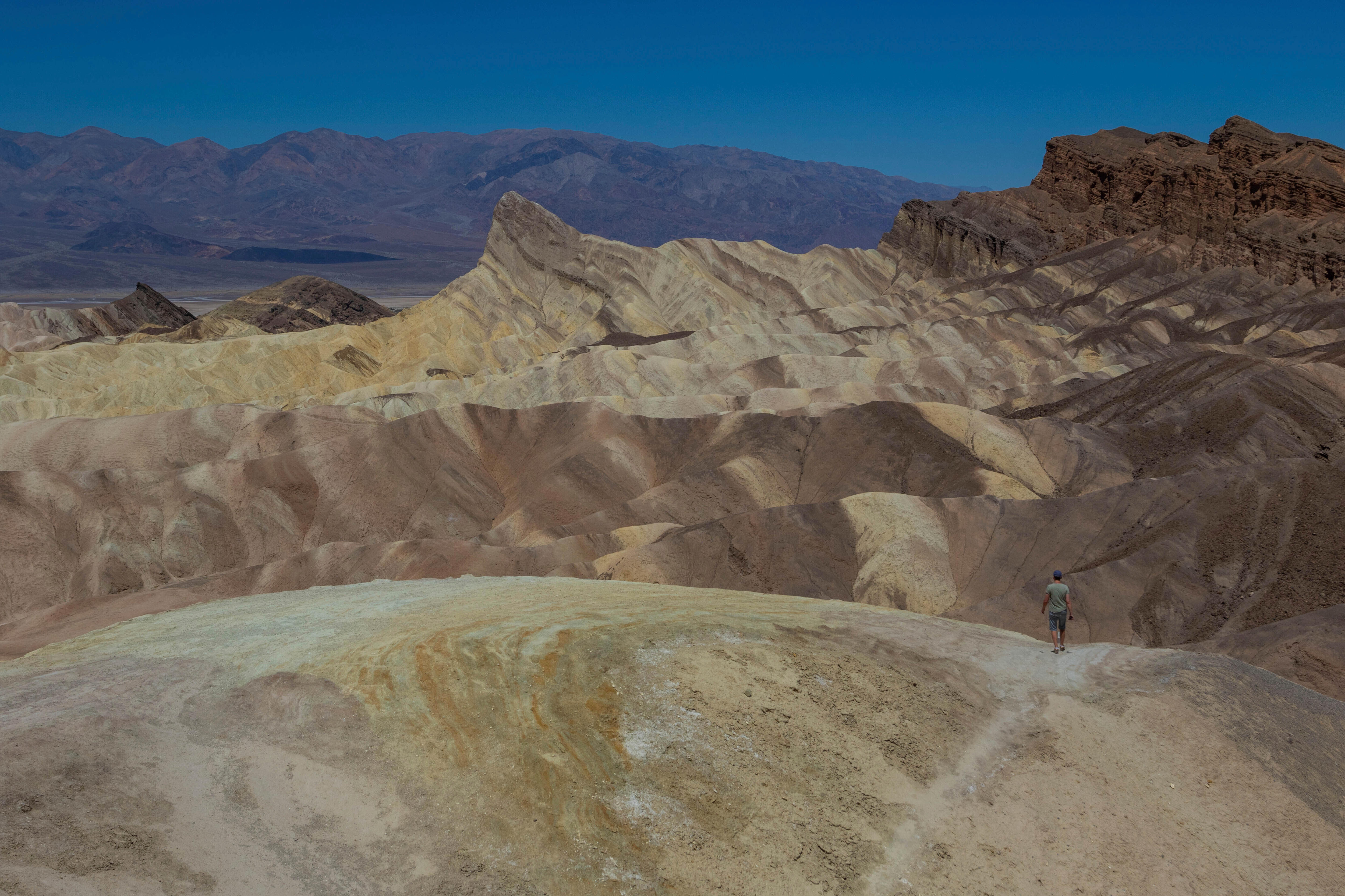 A wide-angle landscape of a mountainous desert landscape with a small figure of a man walking on a hiking path