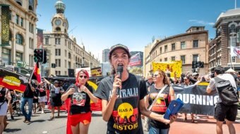 A woman at the head of a march with a microphone wears a t-shirt that reads "Australia has a black history".