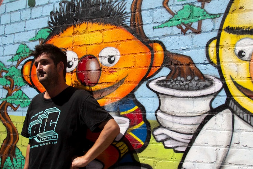 Man leans against a brick wall covered in colourful street art.
