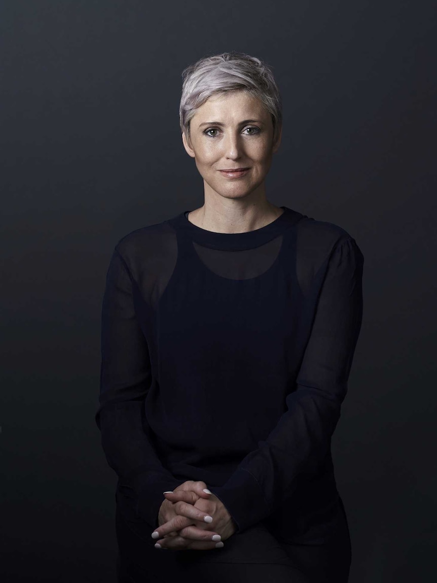 A woman with short hair smiles at the camera against a black backdrop