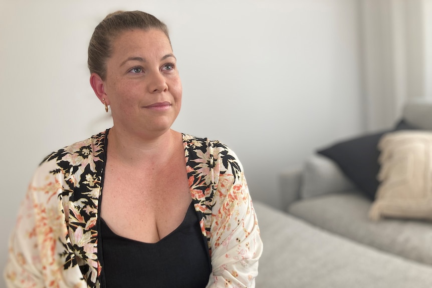 A young woman with her hair pulled back sits inside, looking into the distance, wearing a patterned shirt.