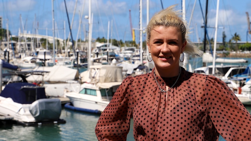 A woman smiling at the camera, standing in front of the water and marina