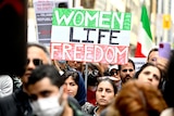 A woman holds a sign saying 'women, life, freedom'.