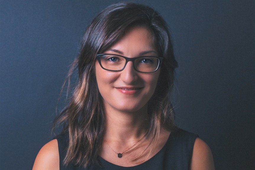 Monash Unversity lecturer Susan Baidawi smiles for an official photographer against a blue wall.