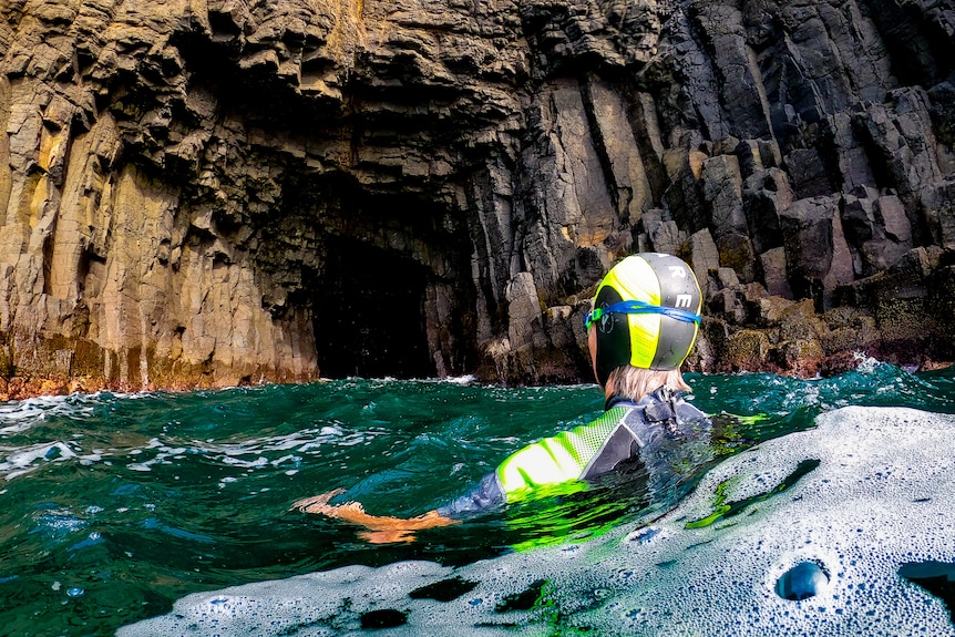 A person swims outside the mouth of the cave below Kiama's blowhole. 