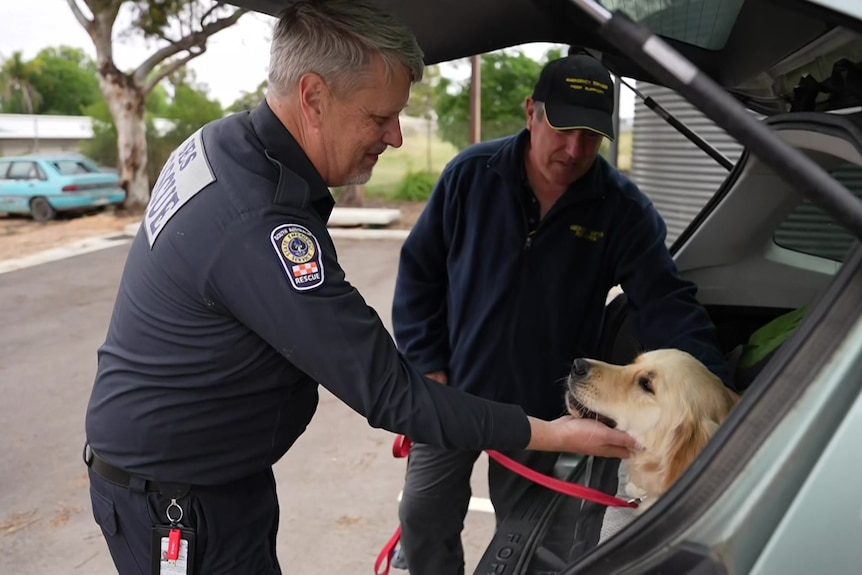 Two men wearing navy blue uniforms pat a dog getting out the back of a car