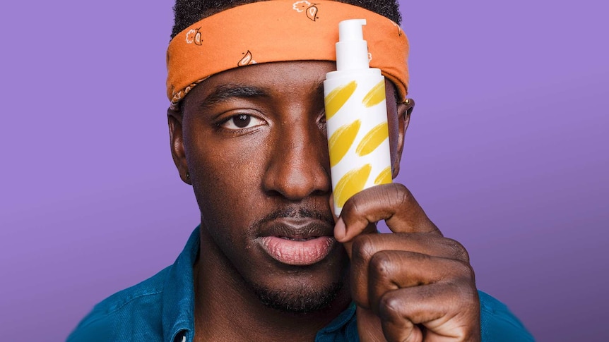 Man with orange headband holding a skincare product bottle in front of his face to depict keeping your skin hydrated in winter.