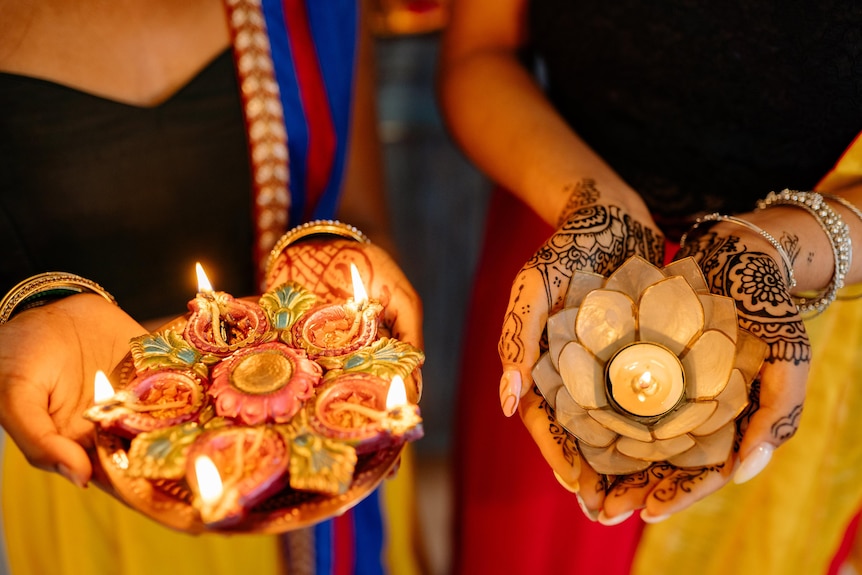 Two people holding out lit clay oil lamps called diyas