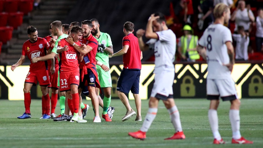 Adelaide United celebrate on the field as Brisbane Roar players look dejected