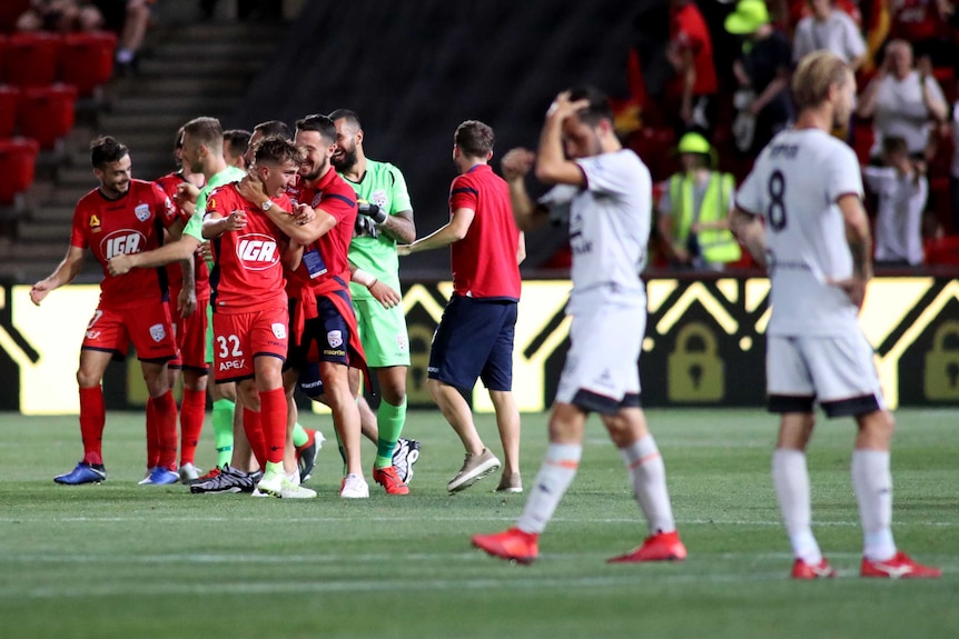Adelaide United celebrate on the field as Brisbane Roar players look dejected