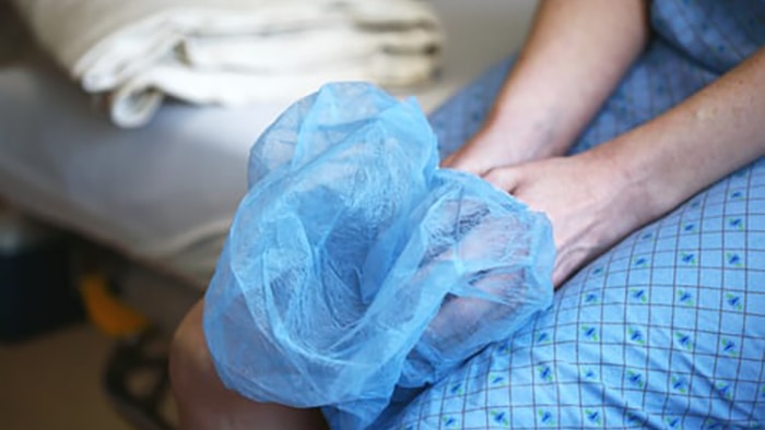 A woman sits on a hospital gurney holding a surgical hairnet