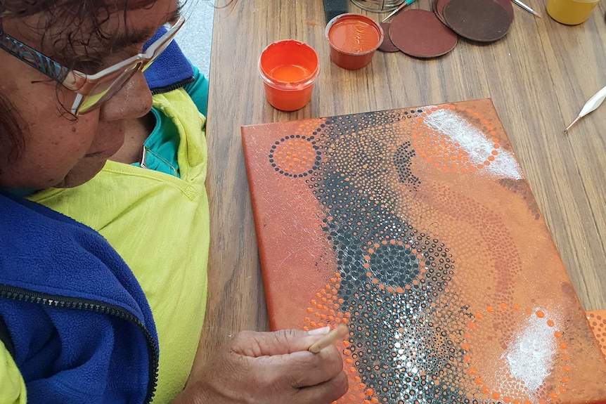 An indigenous woman dot painting using vibrant desert colours at a desk