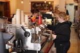 Three women working in a cafe behind a coffee machine.