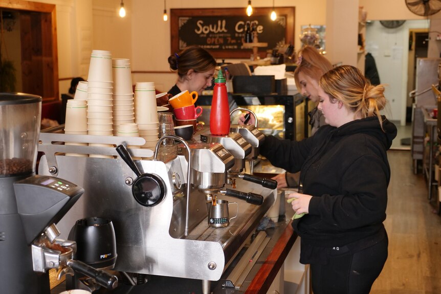 Tres mujeres trabajando en una cafetería detrás de una máquina de café.
