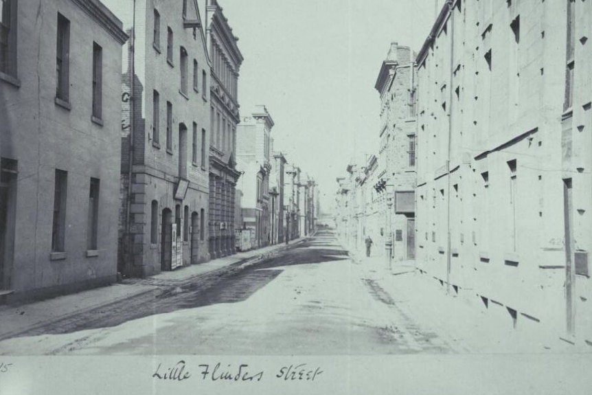 A black and white photo of an almost empty laneway flanked by stone buildings.