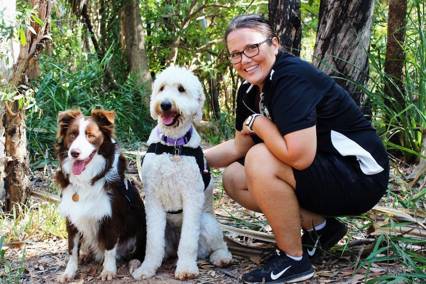 Woman crouching with two dogs in a bush setting.