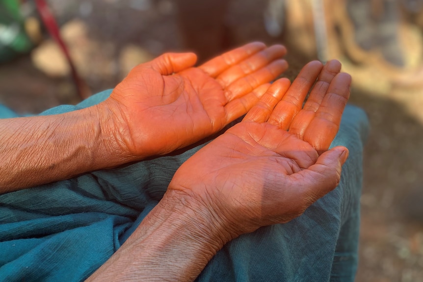 A woman's hands covered in red ochre paint