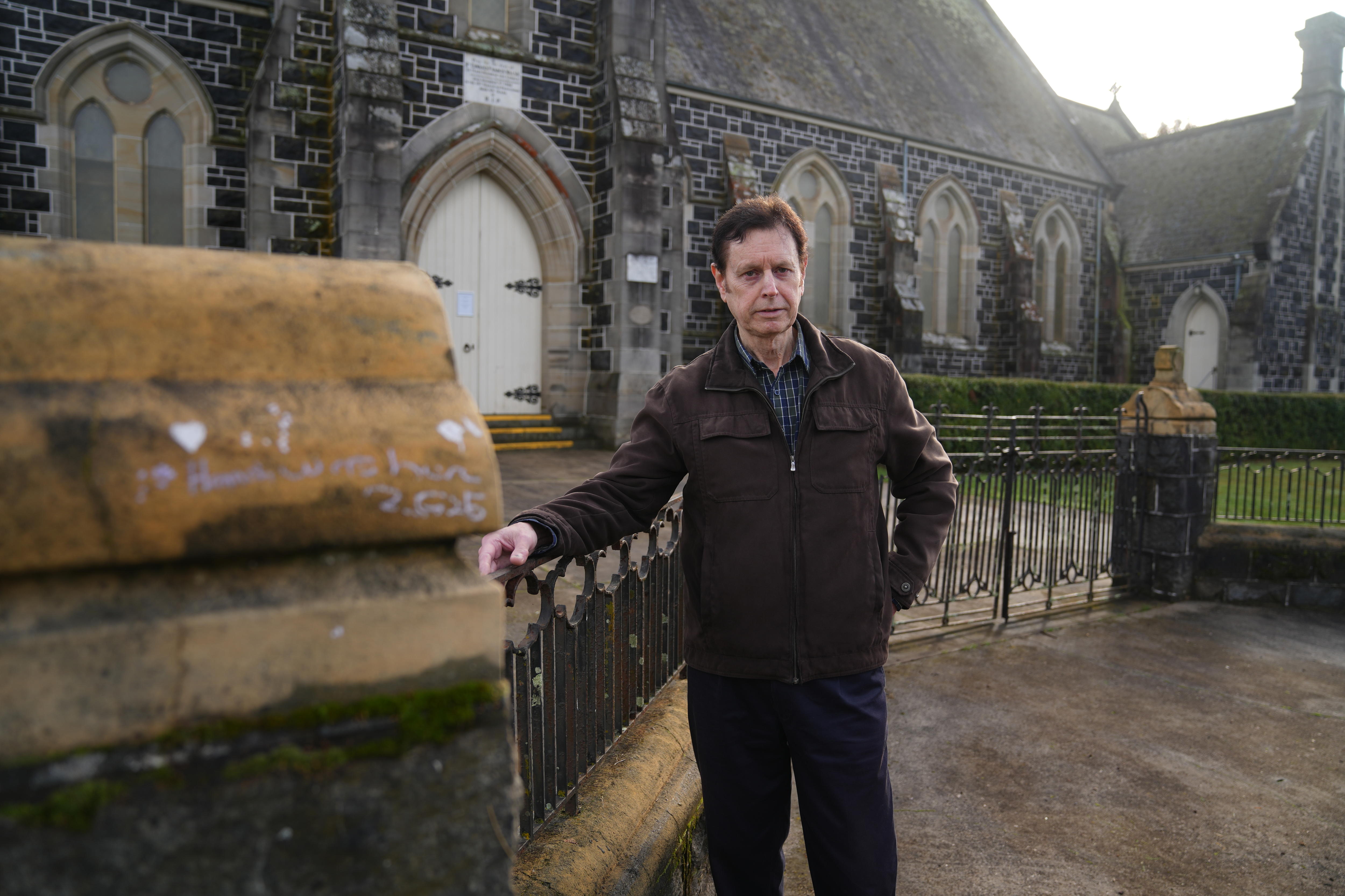 He stands by the Holy Redeemer Catholic Church in Deloraine