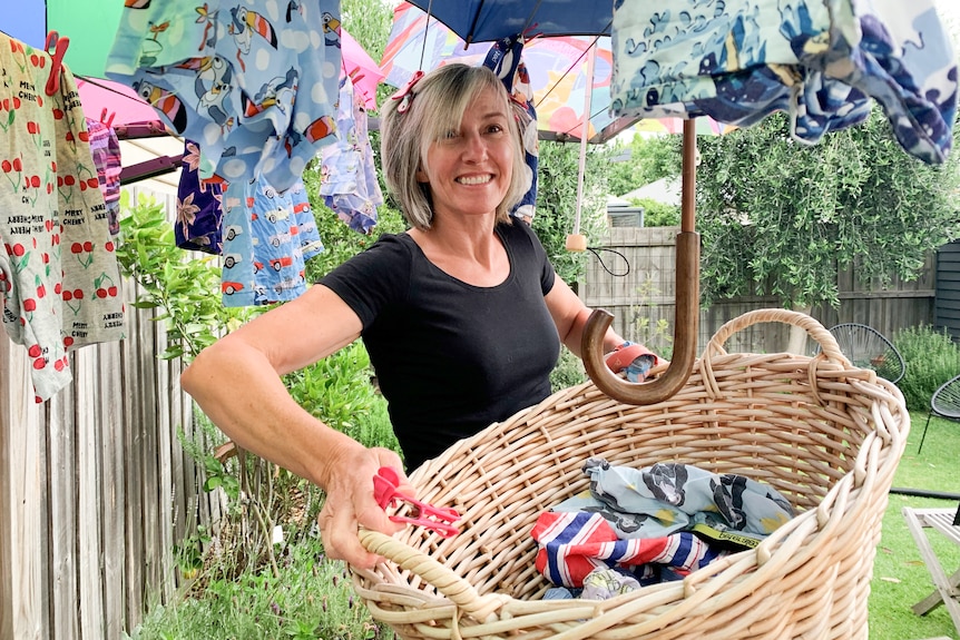 A smiling woman holding a basket of washing while underneath a clothes line