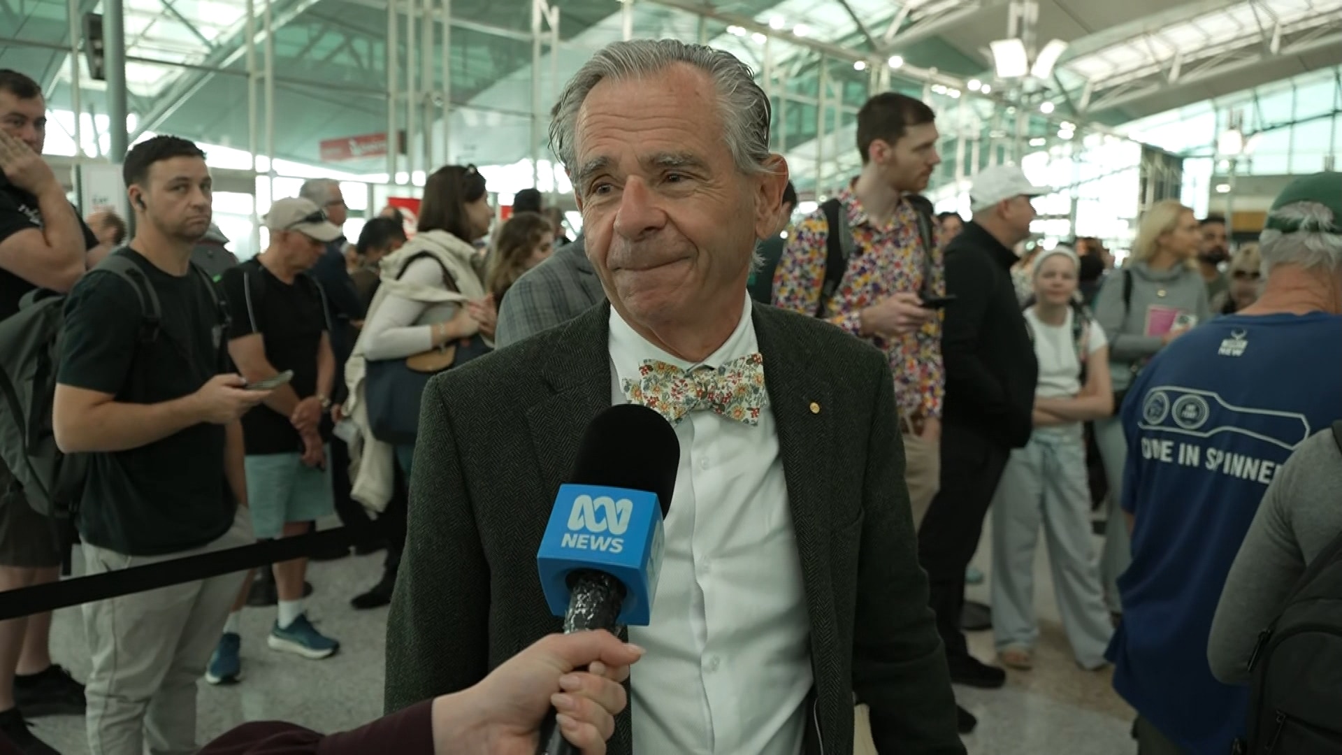 Con smiles in a suit, bow tie, has grey hair, and speaks into a blue ABC microphone.