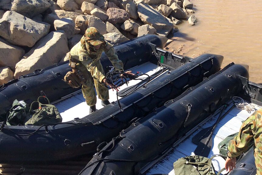 Army officers climb into two zodiac boats on the edge of the water.