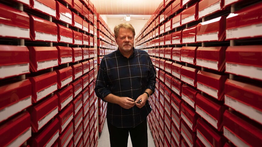 John Huisman stands in an aisle of red shelves.